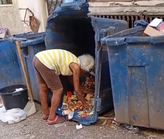 Una anciana rebuscando en un contenedor de basura