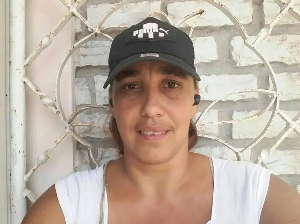 Mujer sonriendo con gorra Puma frente a reja blanca