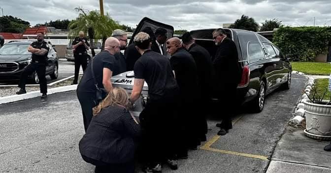 Personas cargando ataúd en coche fúnebre