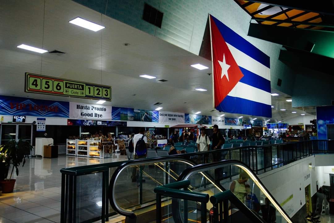 Aeropuerto con bandera cubana y señalización de puertas