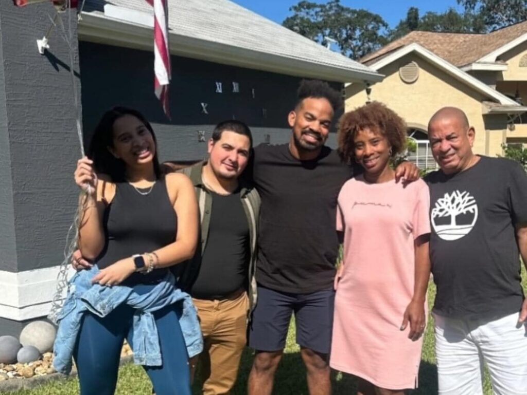 Grupo familiar sonriente frente a casa con bandera