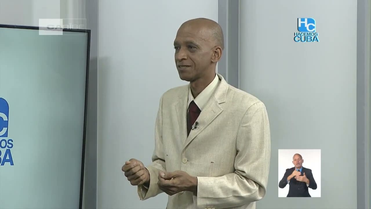 Hombre presentando en programa televisivo con intérprete de señas