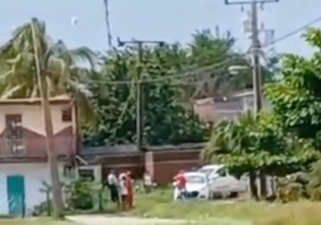 Vecindario tropical con personas alrededor de un coche.