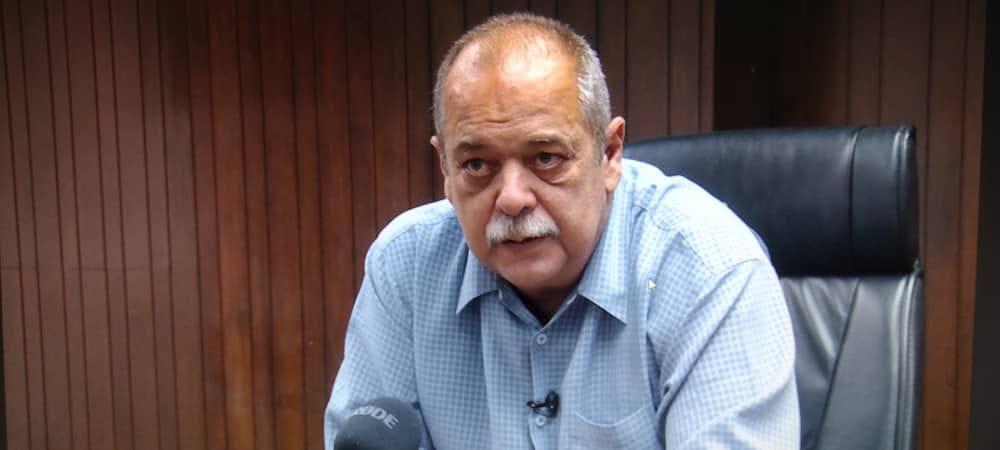 Hombre mayor en entrevista, camisa cuadros, fondo madera