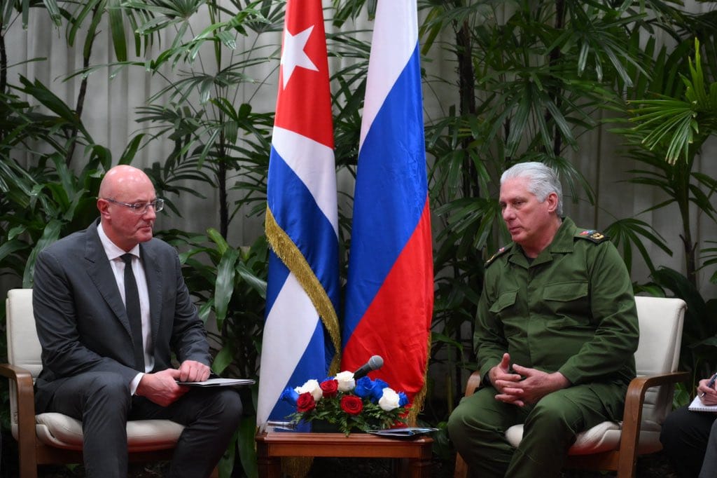 Dos hombres sentados junto a banderas de Cuba y Rusia