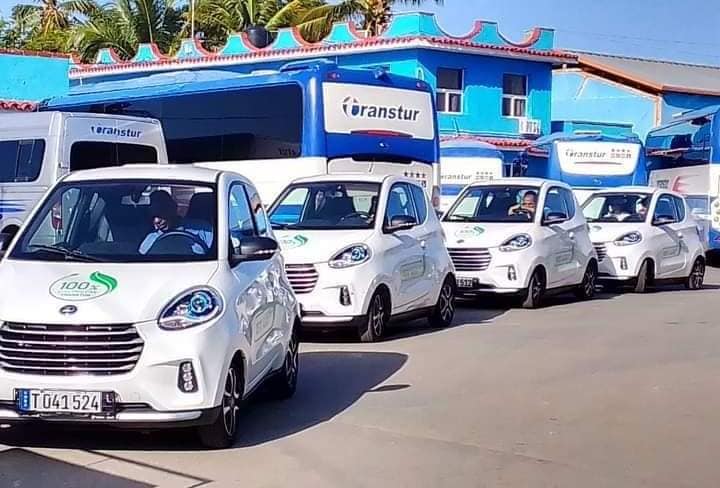 Vehículos eléctricos y autobuses estacionados ante edificio azul