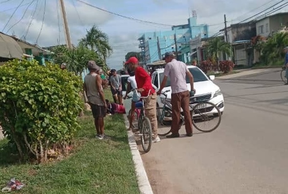 Personas hablando en calle con bicicleta y auto