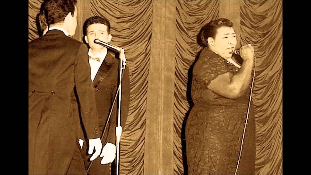 Dúo cantando en escenario con cortinas elegantes