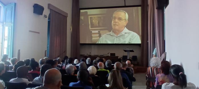 Público asistiendo a una conferencia con video proyectado