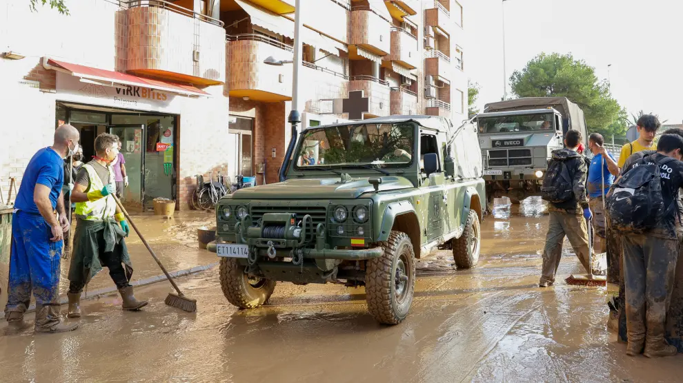 Voluntarios limpiando calle inundada junto a vehículos