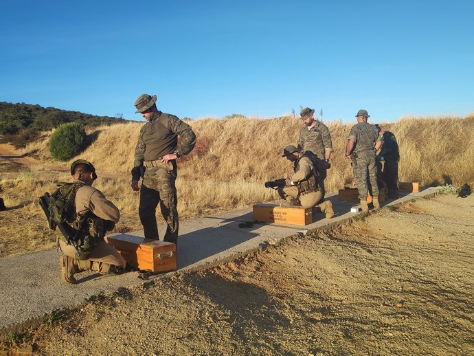 Soldados equipados preparándose en campo al atardecer