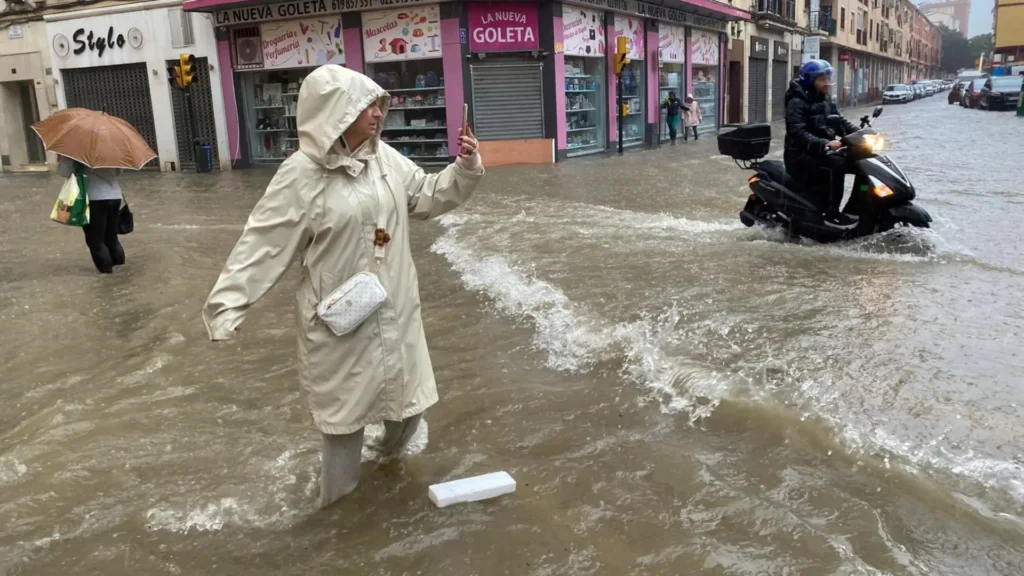 Personas caminando y en moto en calle inundada