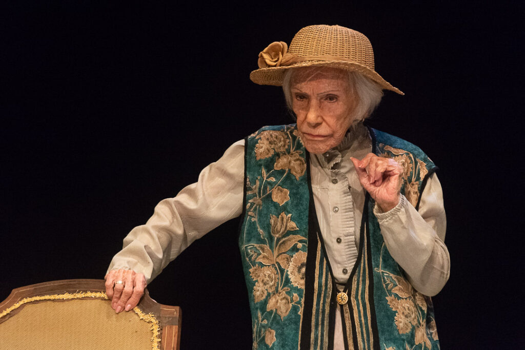 Anciana actuando en teatro con sombrero y chaqueta floral