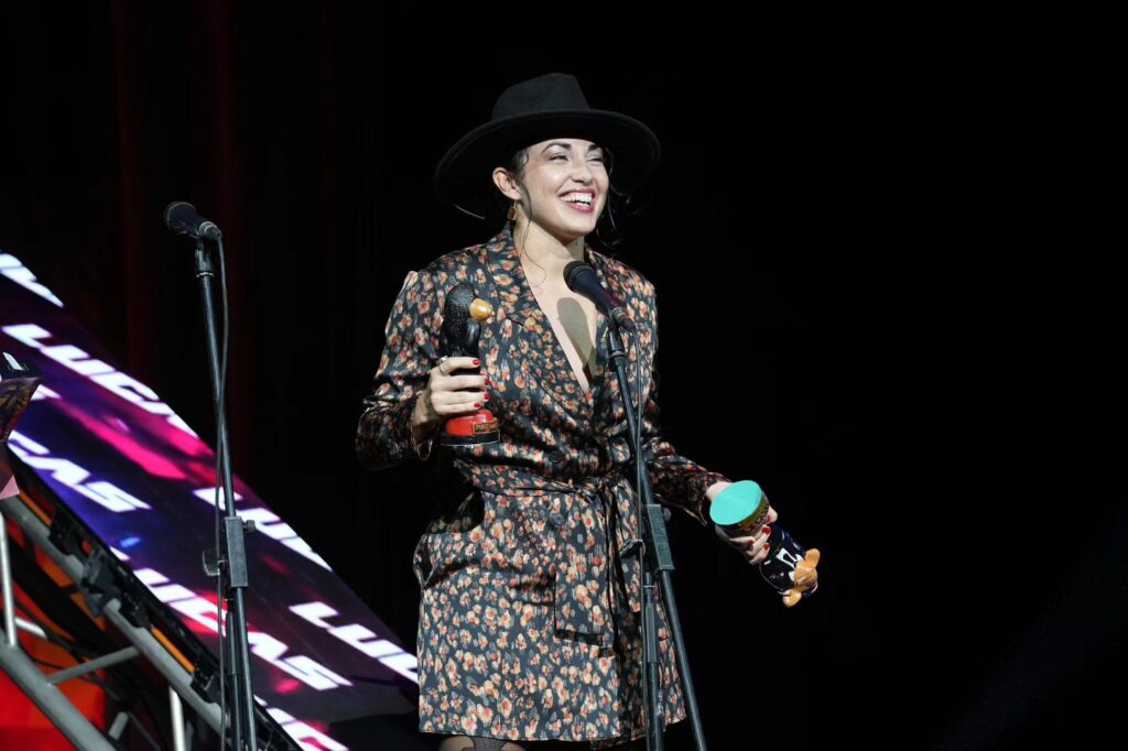 Mujer sonriente con sombrero recibiendo premio en escenario