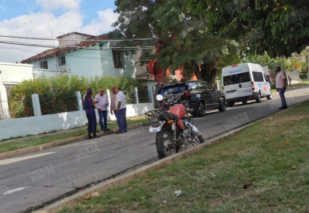 Personas conversando junto a motocicleta en calle arbolada.