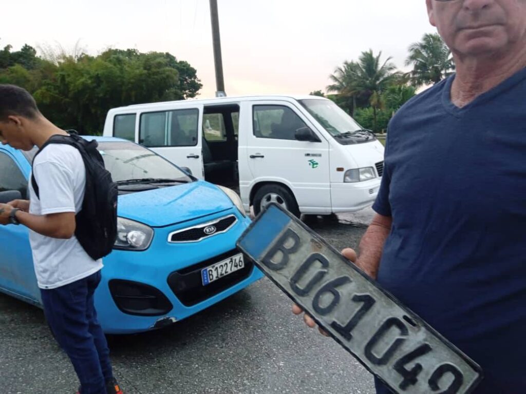 Hombre sostiene matrícula delante de coches dañados