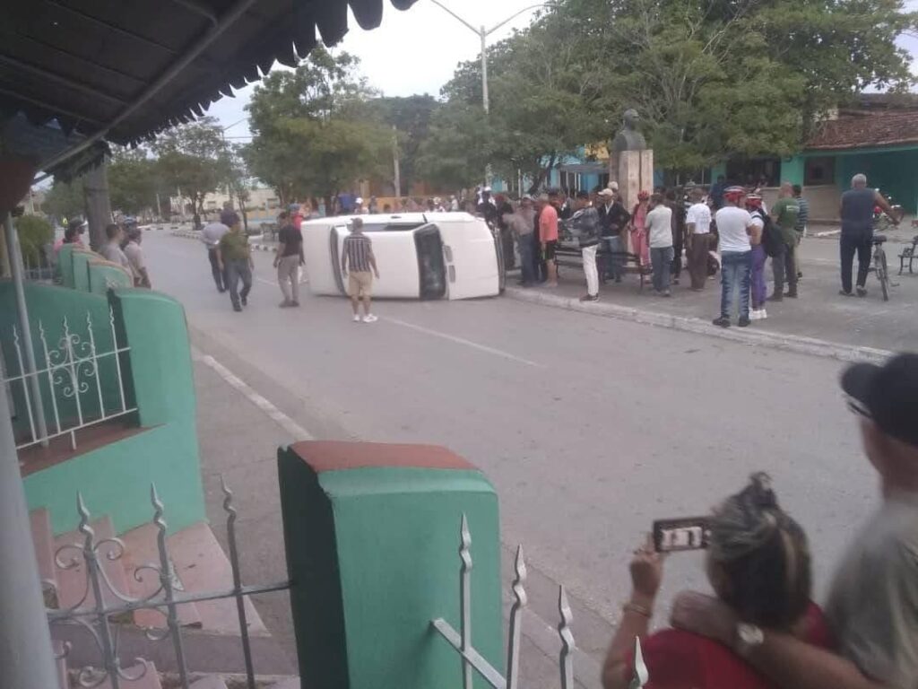 Gente alrededor de coche volcado en calle