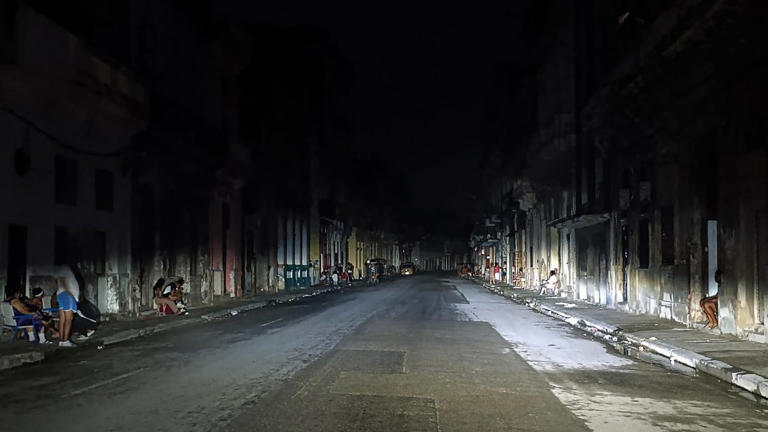 Calle oscura en la noche con personas sentadas
