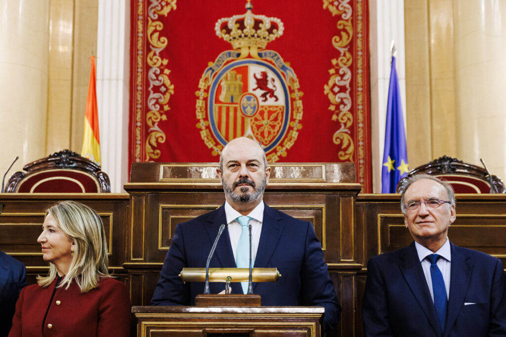 Hombre hablando en podio, bandera España detrás