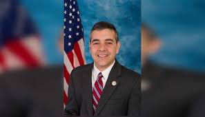 Hombre sonriente con traje frente a bandera estadounidense