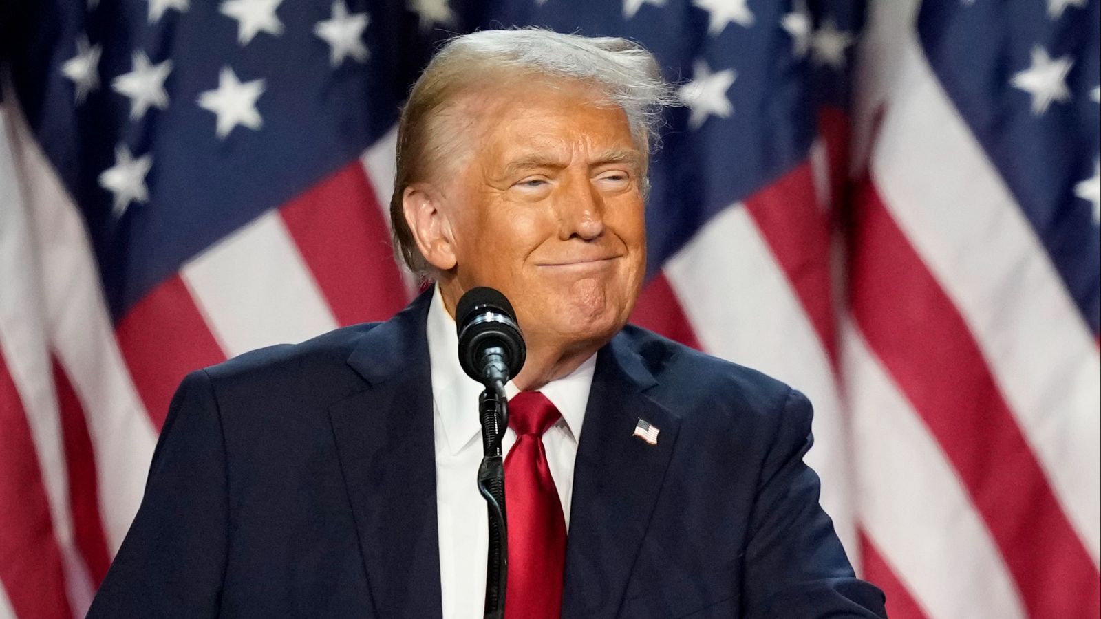 Hombre sonriente dando discurso con banderas de fondo