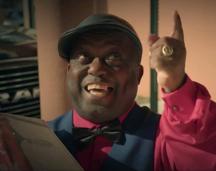 Hombre sonriente con gorra y camisa roja señalando arriba