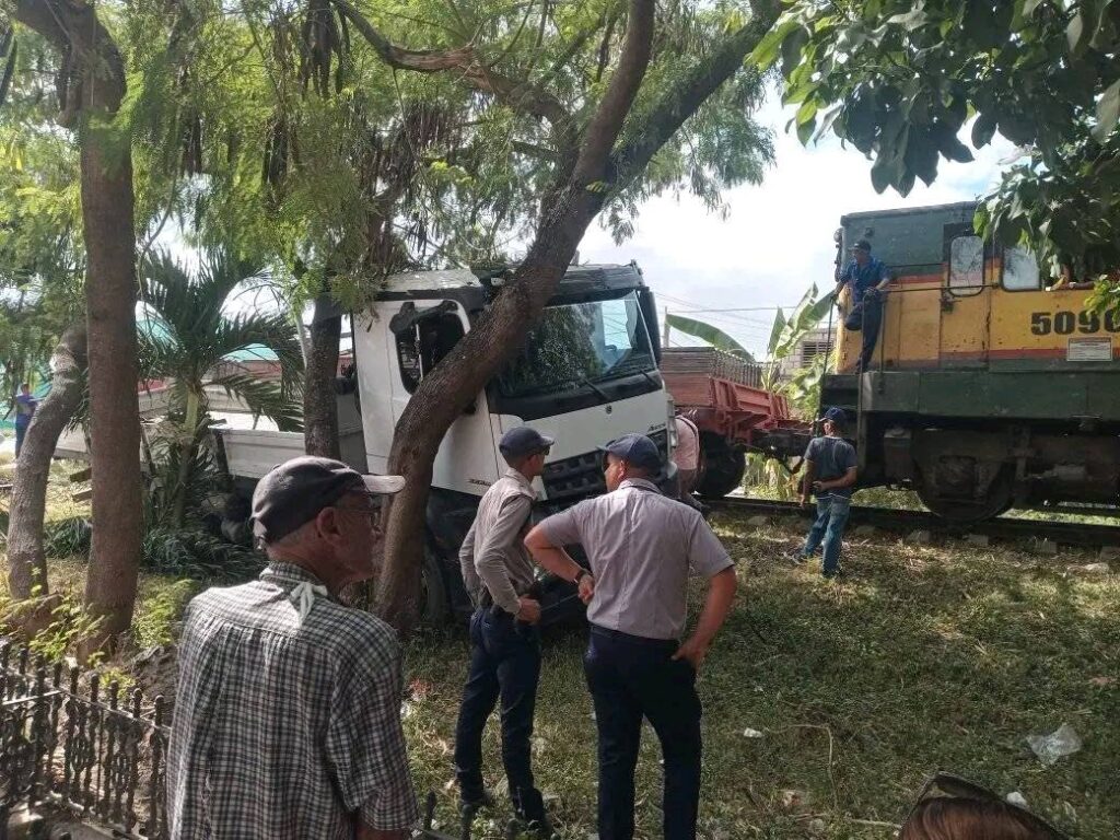Camión accidentado junto a locomotora, personas observando