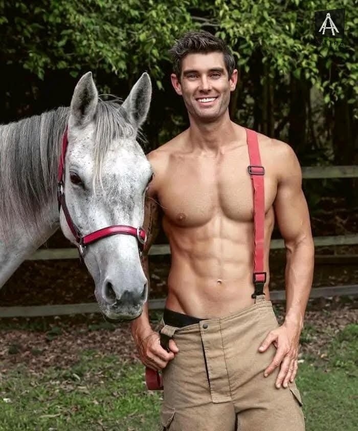 Hombre sonriente sin camisa junto a caballo gris