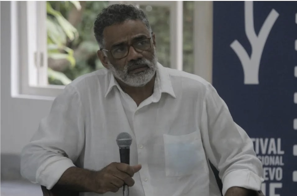 Hombre mayor con camisa blanca hablando en micrófono