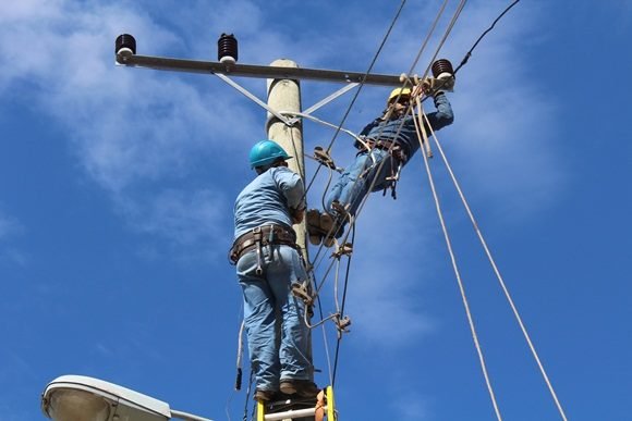Técnicos reparando líneas eléctricas en poste alto