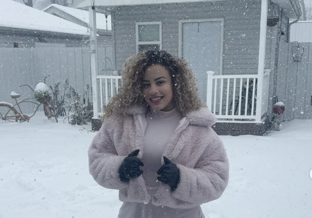 Mujer sonriente bajo nieve con abrigo rosa