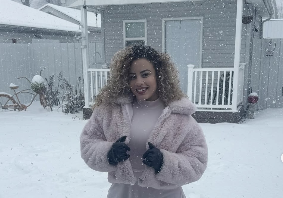 Mujer sonriente bajo nieve con abrigo rosa