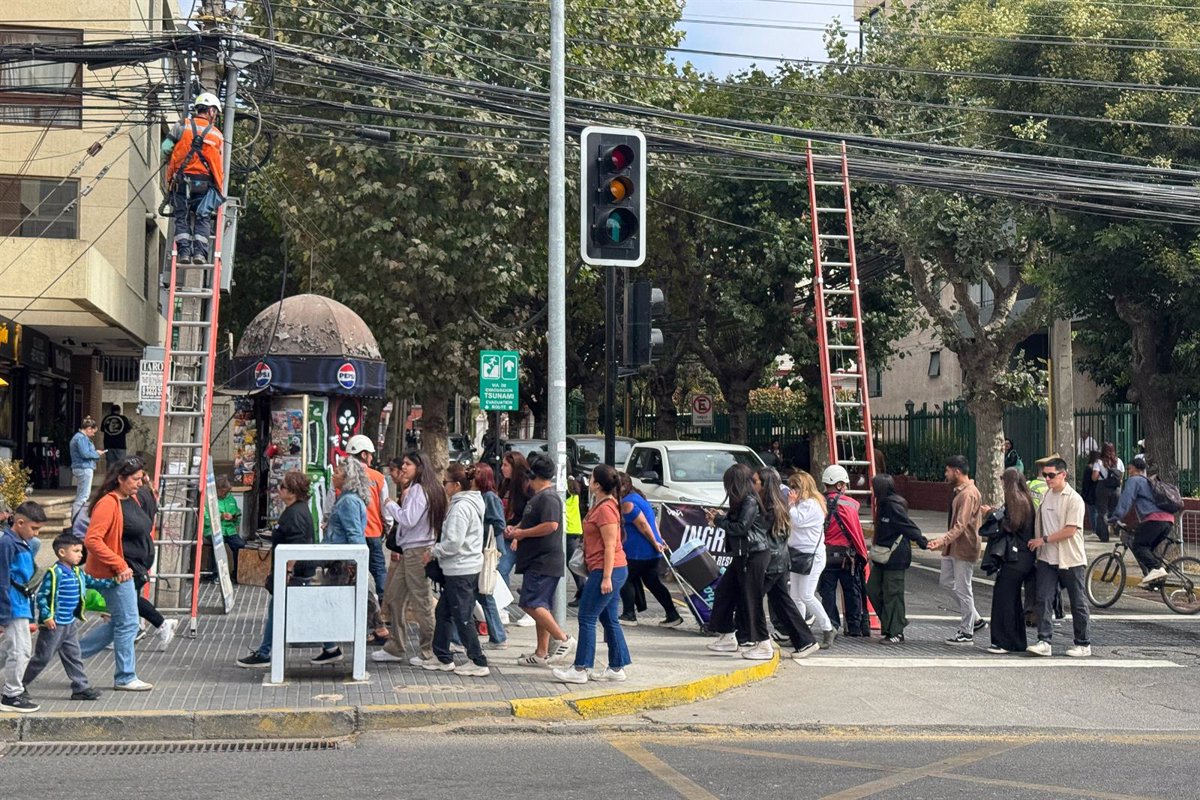 Personas cruzando calle con semáforo y trabajador en escalera