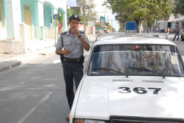 Policía hablando por radio al lado de un coche