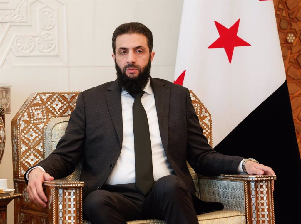 Hombre con barba y traje junto a bandera