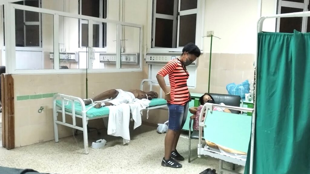 Paciente en cama hospitalaria acompañado por dos personas.