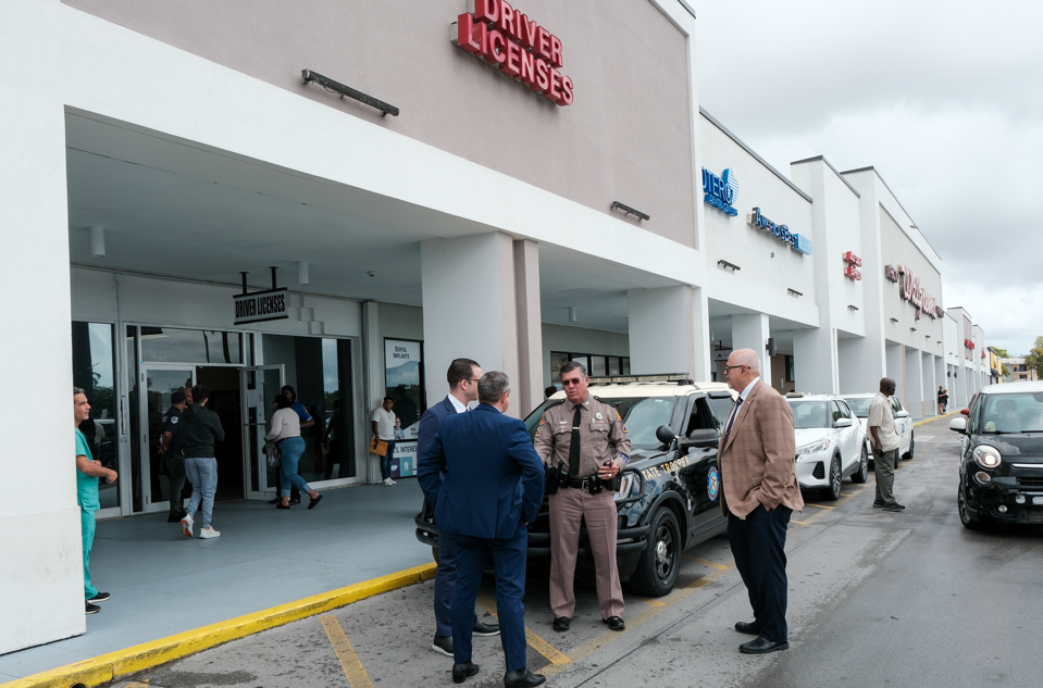 Oficina de licencias con policías y personas afuera.