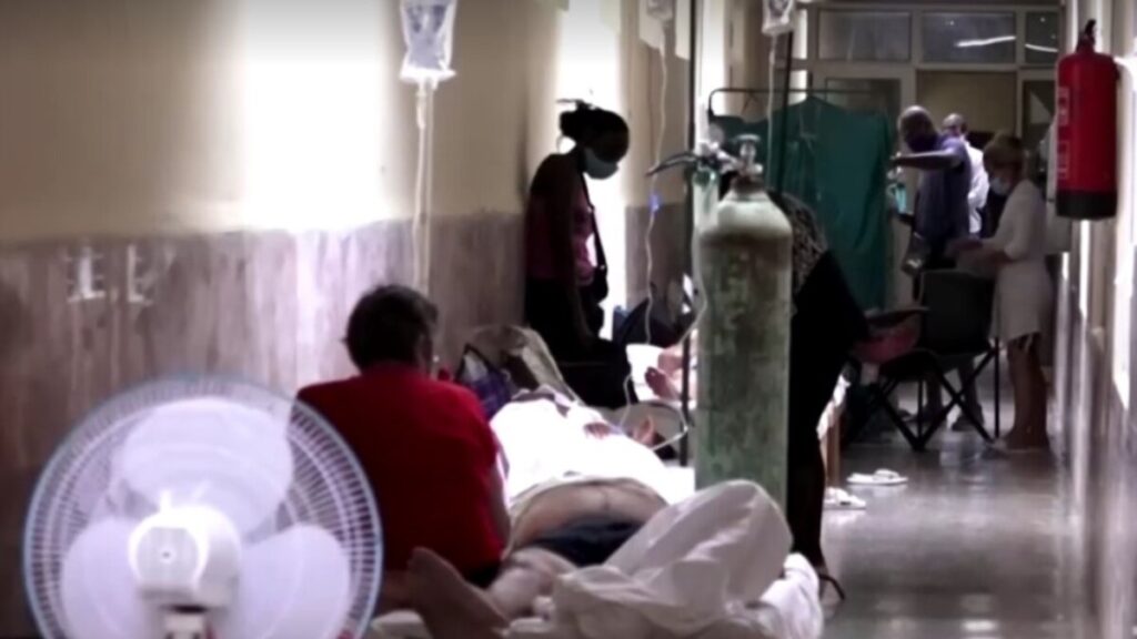 Pacientes en pasillo hospital con oxígeno y ventiladores.