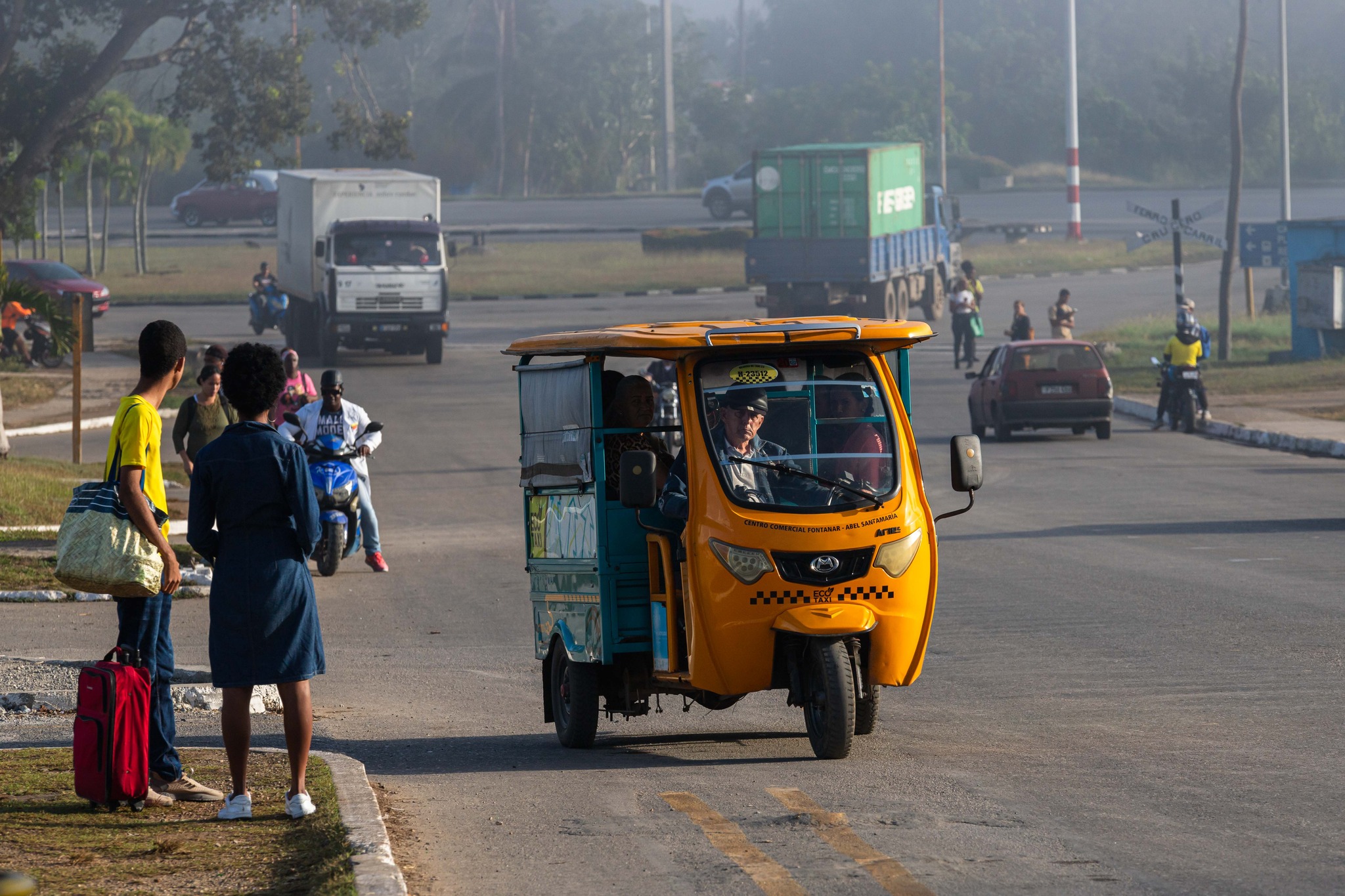 Mototaxi amarillo en carretera transitada con personas.