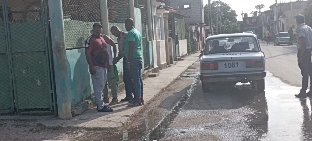 Personas conversando en una calle junto a coche antiguo.