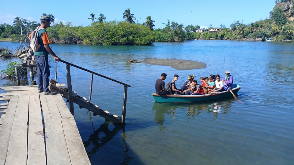 Personas cruzan río en bote cerca de puente.