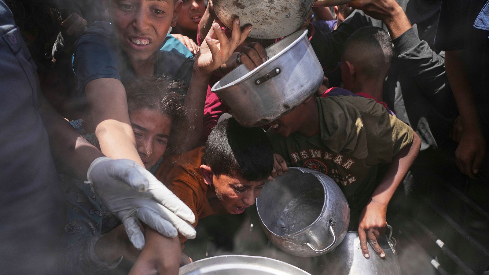 Multitud busca comida en fila con ollas.