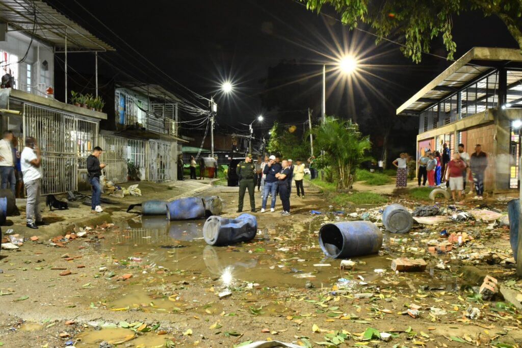 Calle inundada con escombros y personas observando.