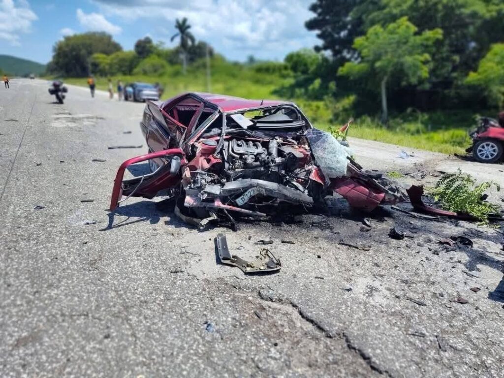 Coche accidentado en carretera abierta, vegetación al fondo.