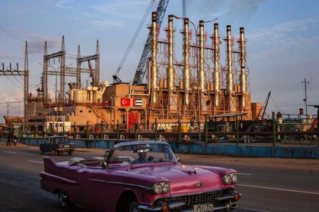 Coche clásico rosa frente a planta eléctrica industrial.