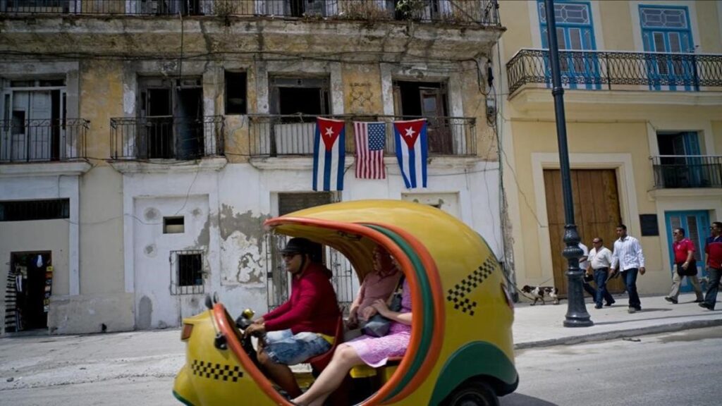 Coche amarillo pasa frente edificio con banderas cubanas.