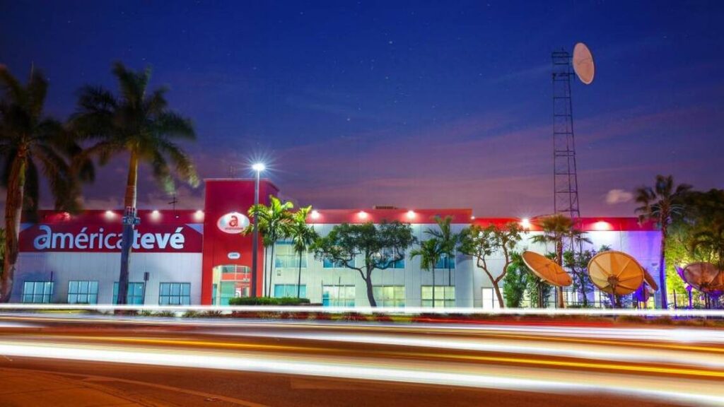 Edificio iluminado, antenas y palmeras de noche.