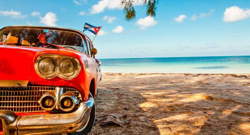 Coche clásico rojo con bandera cubana en playa