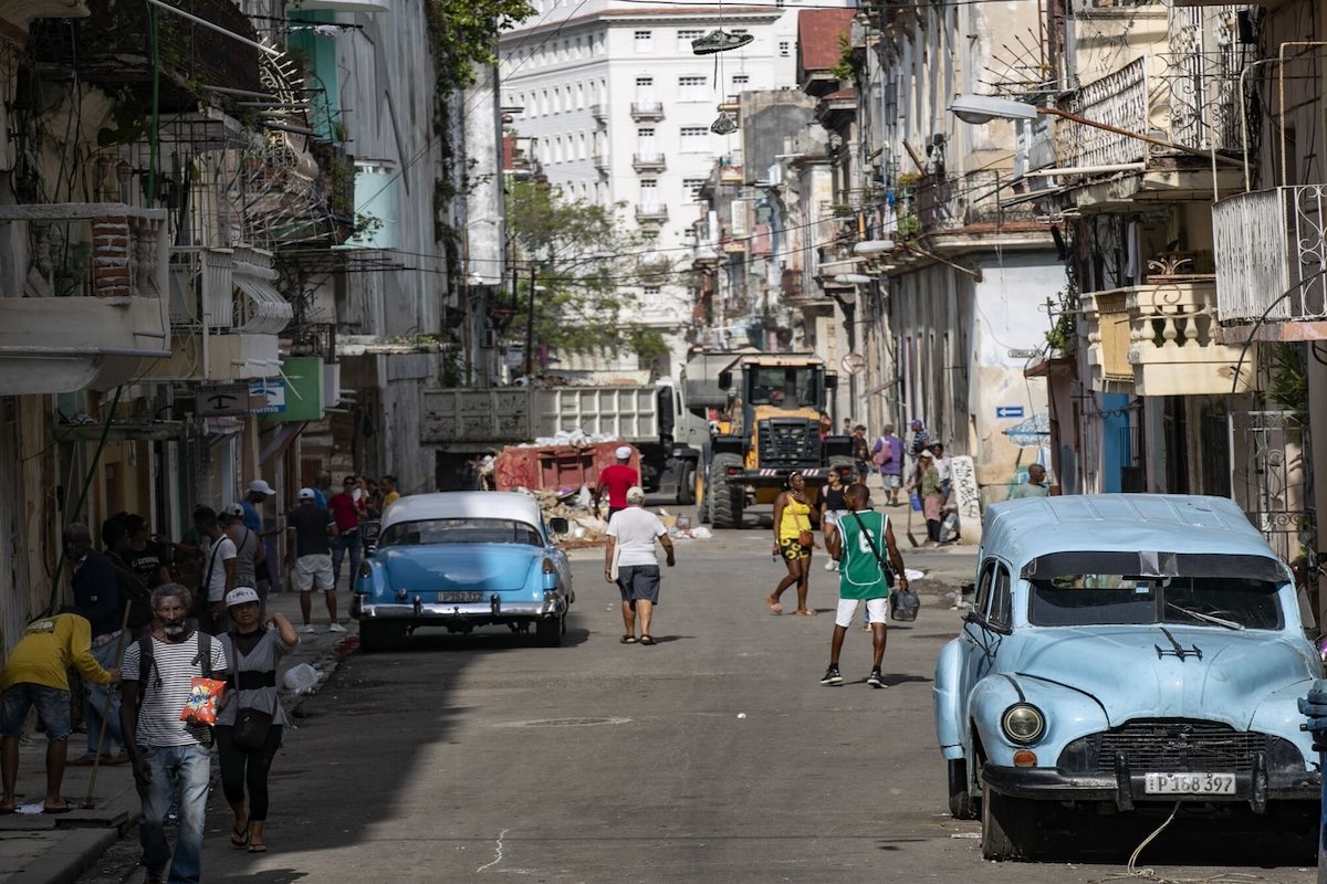Calle con coches antiguos y personas caminando.