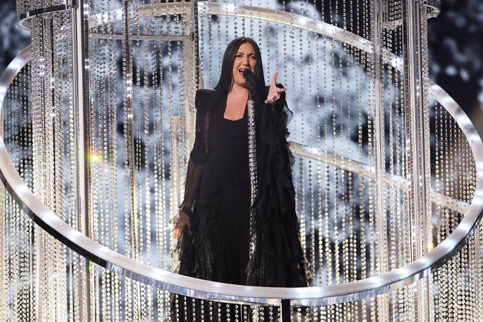 Cantante actuando en escenario iluminado con luces brillantes.